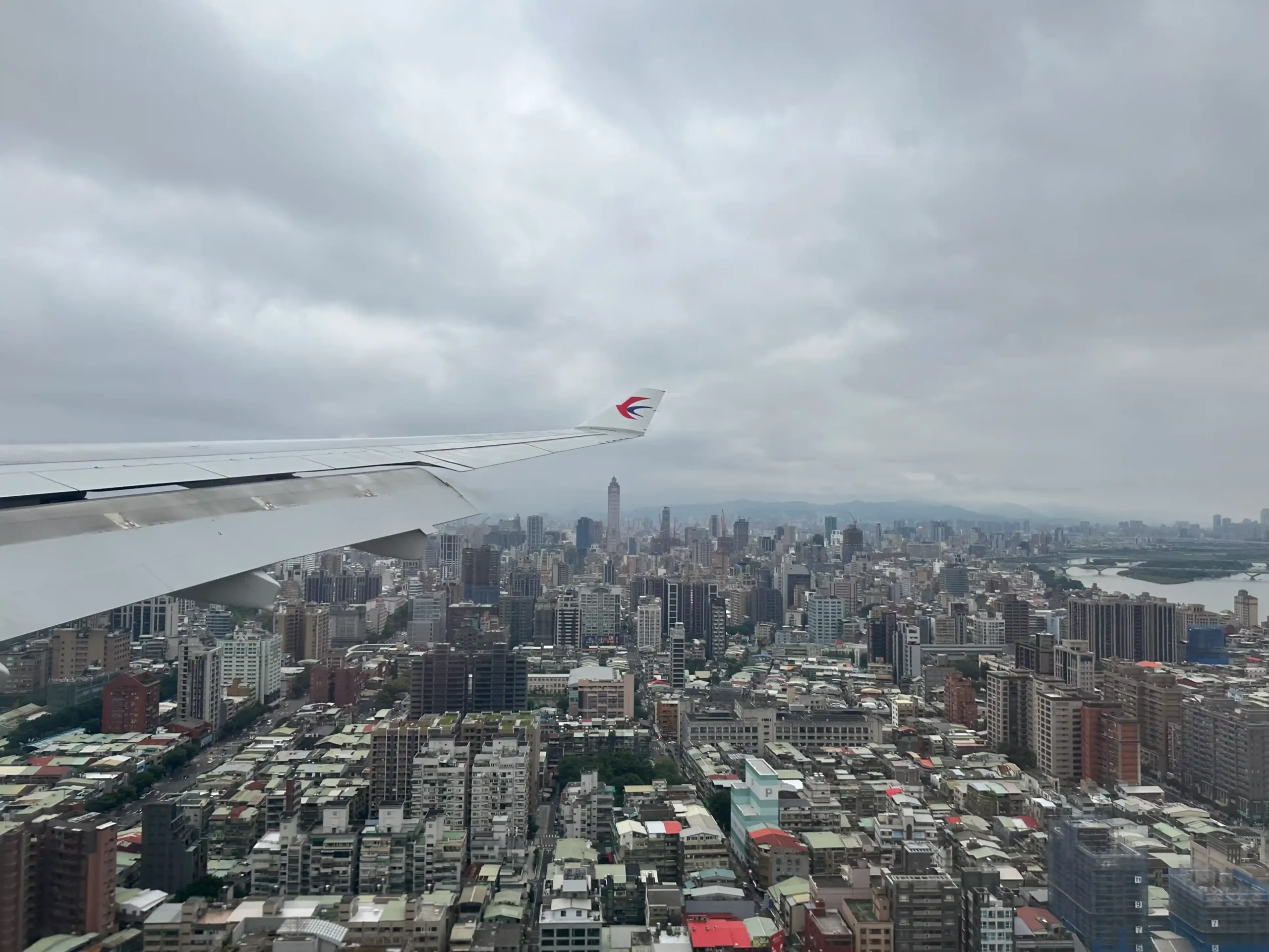 an airplane wing in the air with a city in the background